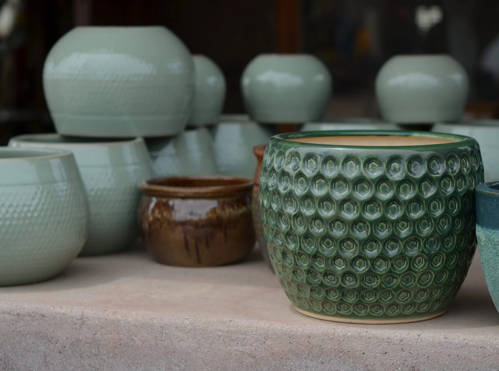 Table topped with a variety of green and brown ceramic pots