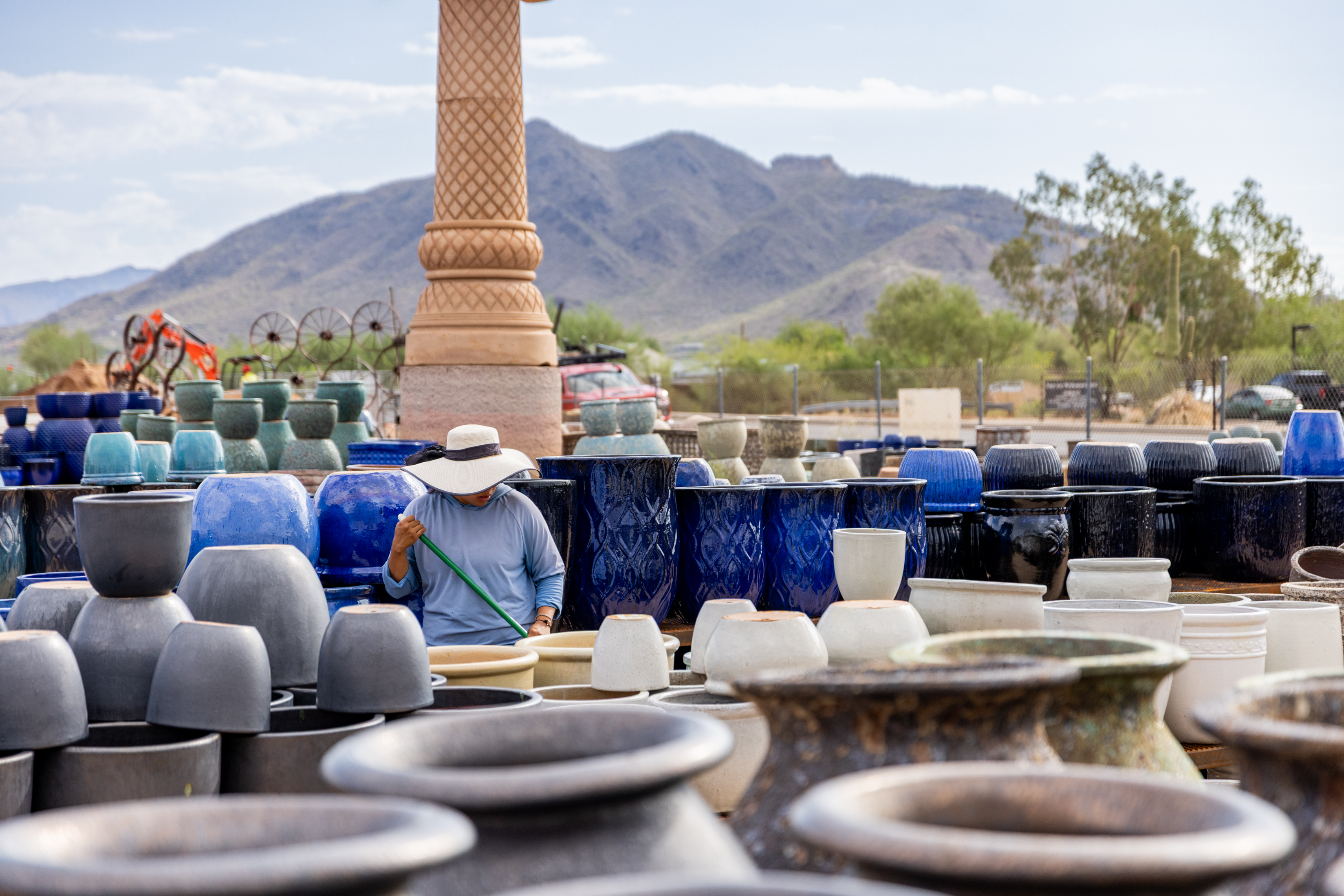 Man wearing a hat and holding a stick, standing in front of a large pile of pottery