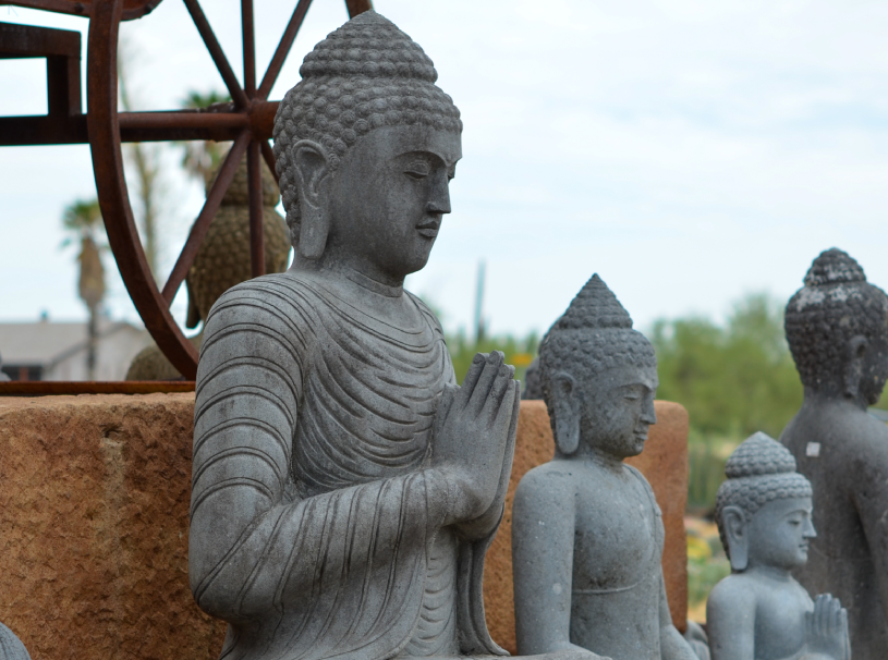 Group of Buddha statues sitting atop a stone wall, surrounded by trees, buildings, and a clear blue sky